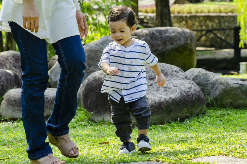 Low section of mother walking with cute boy on grassy land in park