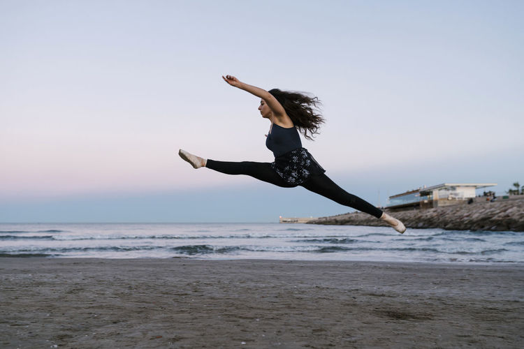 Graceful female ballet dancer with legs apart practicing at beach during sunset