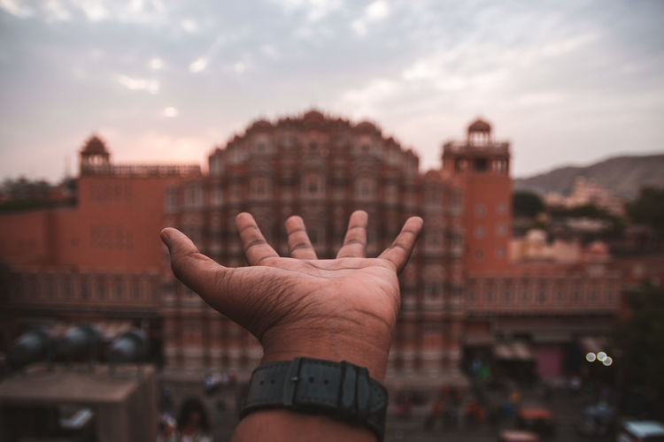 Cropped image of person hand against building in city against sky