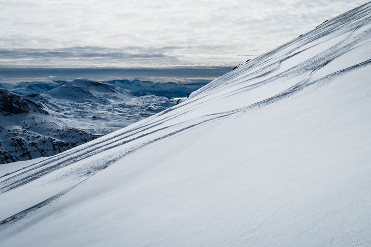 Snow covered mountain with ski tracks against sky 