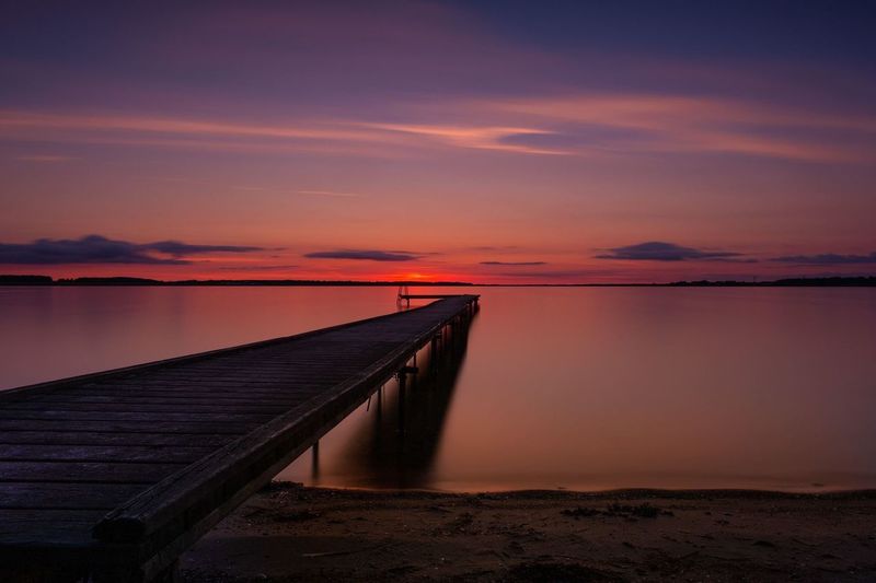 Scenic view of pier over lake against romantic sky during sunset