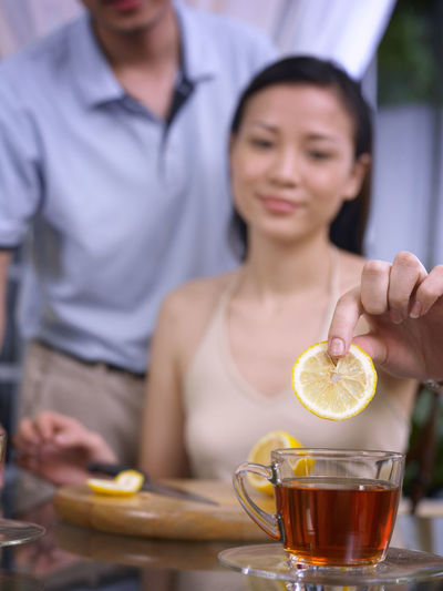 Woman with man adding lemon slice in tea on glass table at home