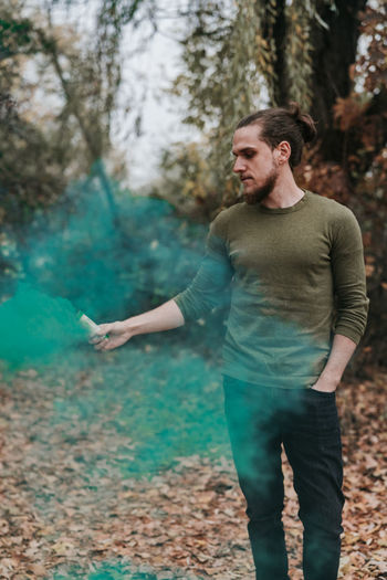 Young man holding distress flare while standing in forest during autumn