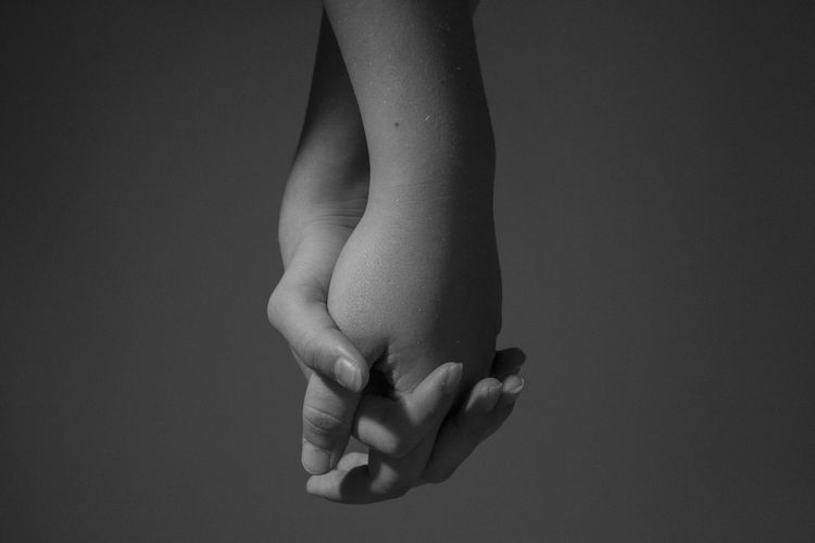 Cropped image of people holding hands against gray background