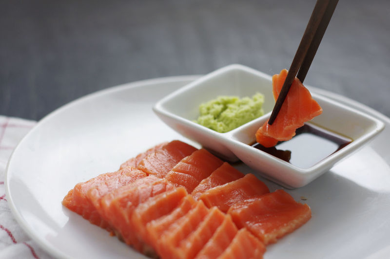 Close-up of chopsticks dipping salmon sushi in soy sauce