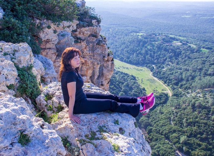 Full length of young woman relaxing on rocky cliff