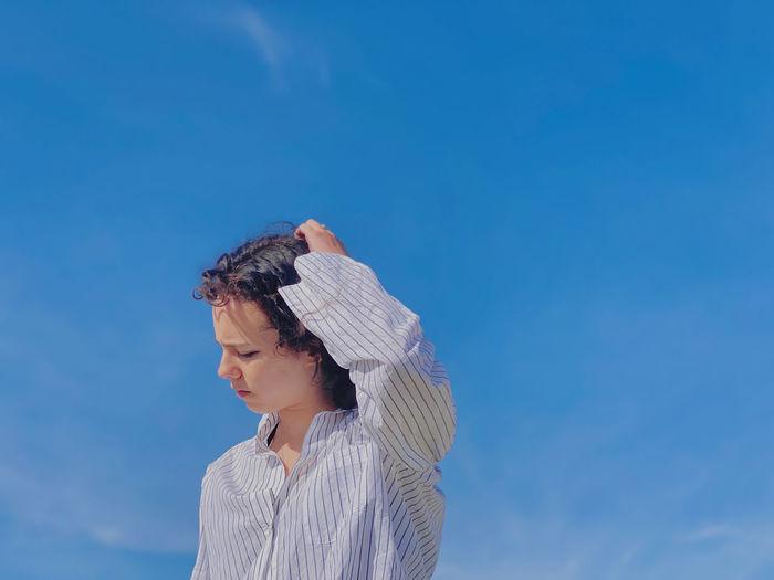 Low angle portrait of young woman standing against blue sky