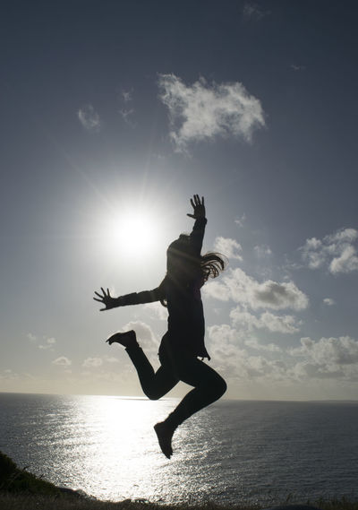 Silhouette woman jumping on beach against sky during sunset