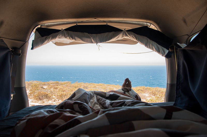 Person sleeping in van by sea against sky