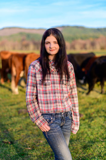 Young woman standing on field by cattle
