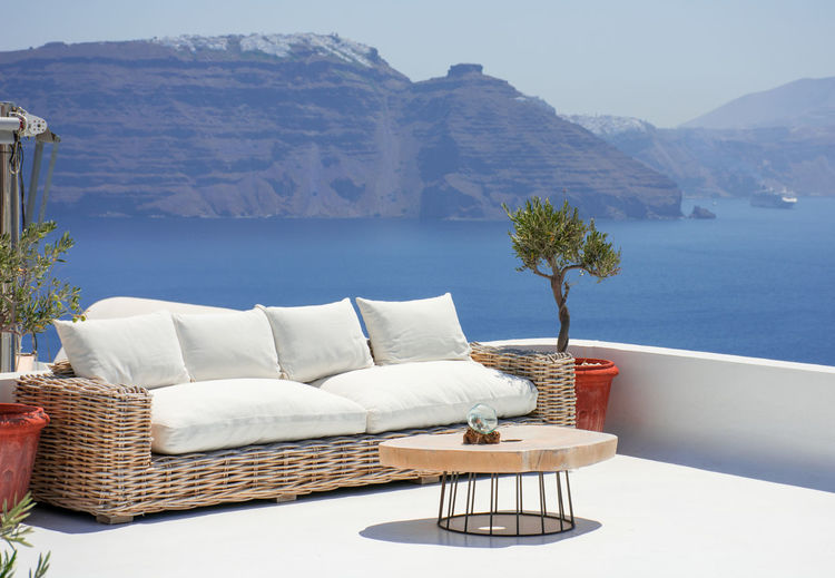 Beautiful terrace with couch and a small table in the village of oia in the greek island of santorini. nobody is enjoying now the spectacular panoramic to the cliff with fira at the top. hori