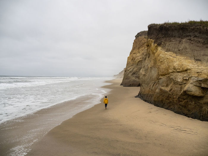 Lone young person walking along deserted california beach on gray day