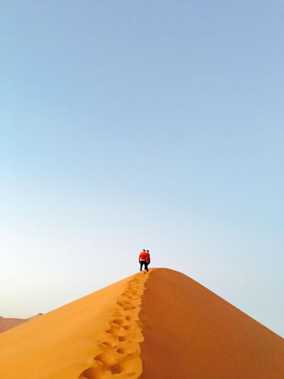 People walking on desert against clear sky