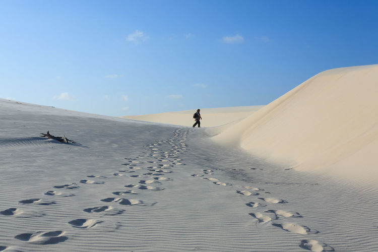 Man walking on sand dunes at desert against sky