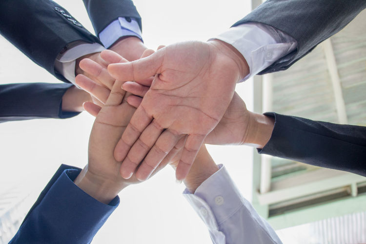 Cropped hands of business people huddling against sky