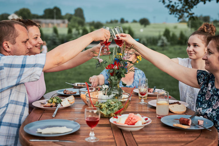 Family making toast during summer picnic outdoor dinner in a home garden