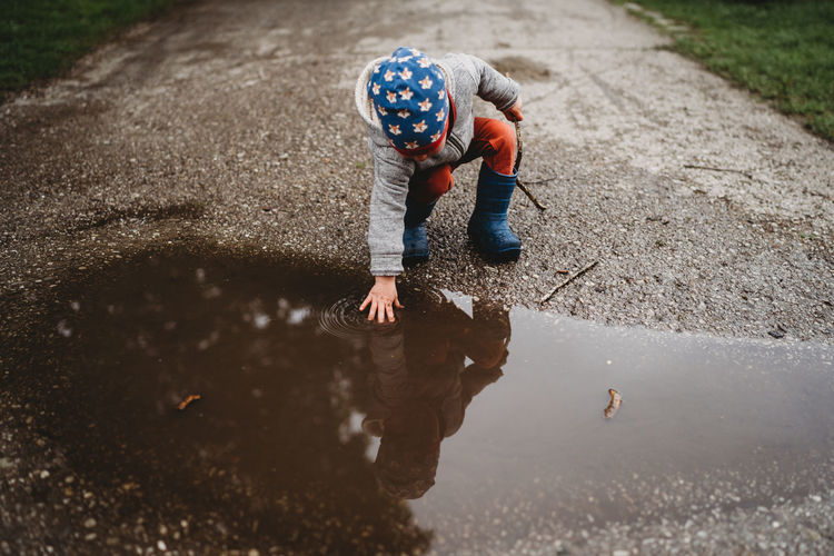 Young male toddler putting hand in a puddle at the park on cloudy day