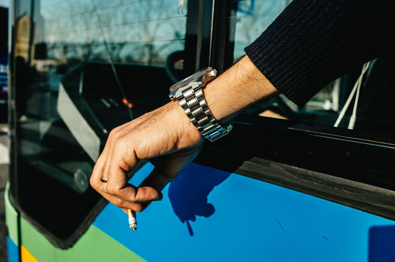 Cropped hand holding burnt cigarette on sunny day in bus
