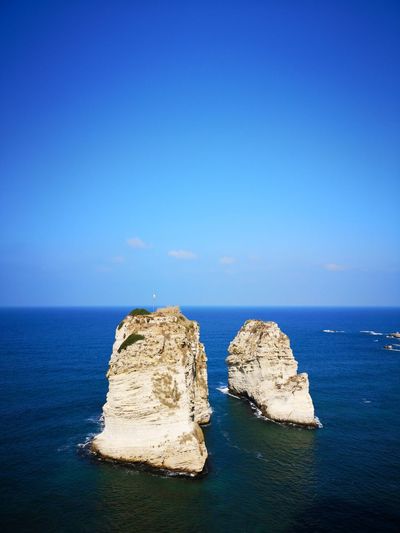 Rock formation in sea against clear blue sky