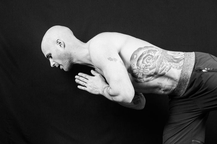 Shirtless bald man doing yoga against black background