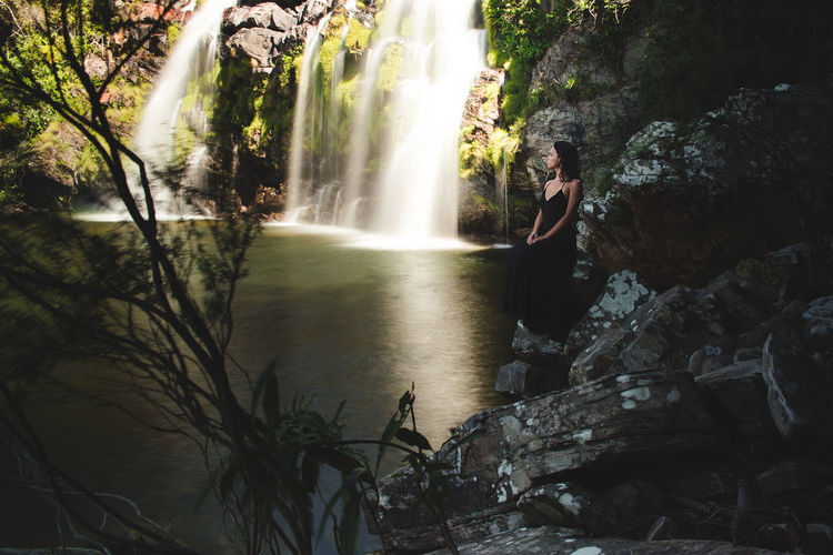 Woman standing on rock by waterfall in forest