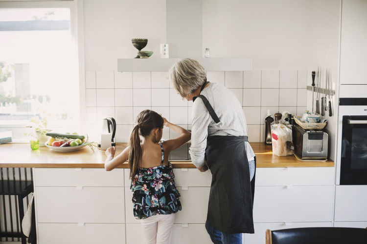 Rear view of girl standing with grandmother preparing food in kitchen