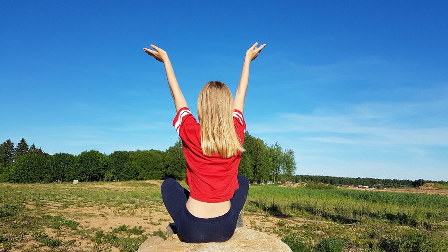 Woman with arms raised on field against blue sky