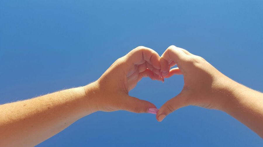 Close-up of hands showing heart shape against sky