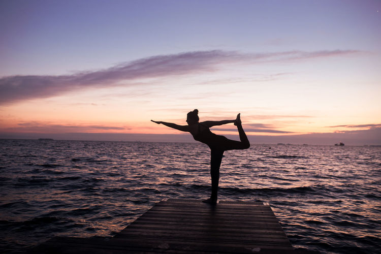 A woman practicing yoga at the seaside in the sunrise golden hour ,silhouette
