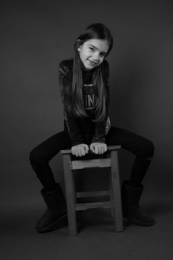 Portrait of smiling girl sitting on chair against black background