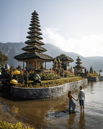 From above young couple walking on brown river stream near buddhist temples in flower garden on with cloudy sky in indonesia