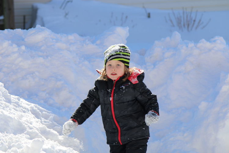 Cute girl wearing padded jacket and knit hat playing in snow