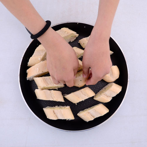 Cropped image of woman arranging garlic bread in frying pan over white background
