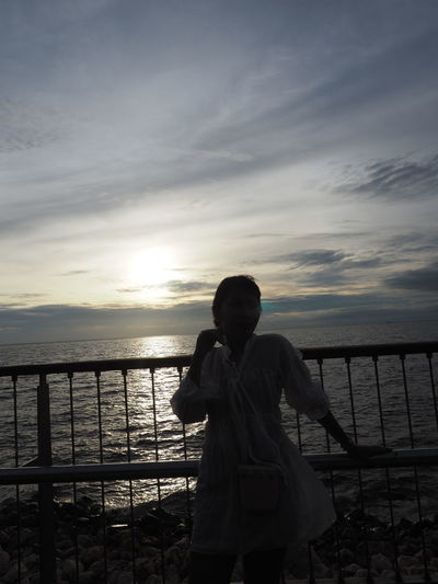 Man standing on railing against sea during sunset
