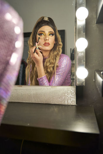 Non binary person doing make-up looking at mirror