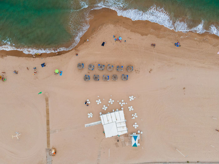 Magnificent aerial view of turquoise sea waving on sandy coastline with deckchairs and umbrellas in summer