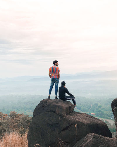 Men sitting on rock looking at mountain against sky