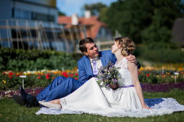 Bride and bridegroom sitting on picnic blanket at park