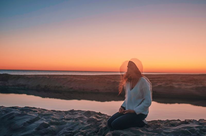Multiple image of woman sitting on rock by sea against sky during sunset