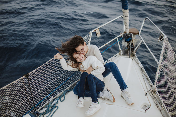 Happy mother and daughter sitting on sailboat during vacations