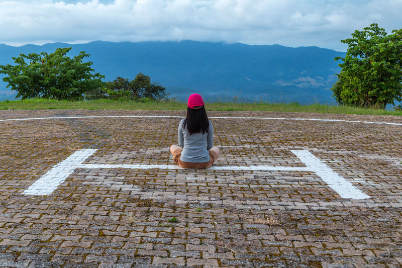 Rear view of woman sitting on helipad against sky