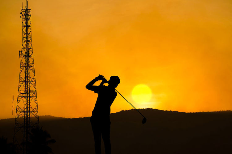 Golfers' hit golf ball toward the hole at sunset silhouetted. 