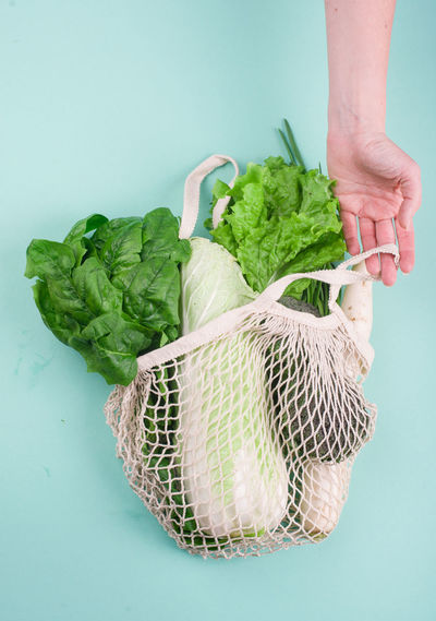 Cropped hand of person holding vegetable basket against blue background