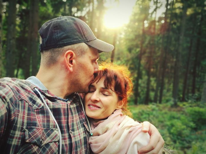 Man kissing on girlfriends forehead while standing in forest