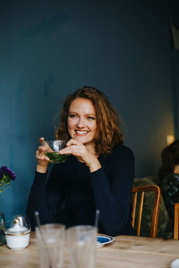 Smiling woman holding herbal tea while sitting at cafe