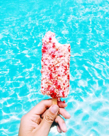 Cropped hand holding popsicle against swimming pool