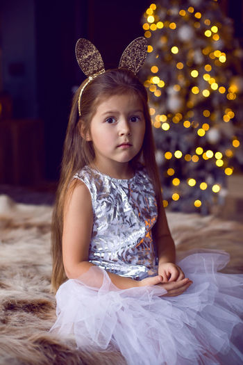 Girl in dress and with bunny ears sitting on bed with fur in studio dress in christmas