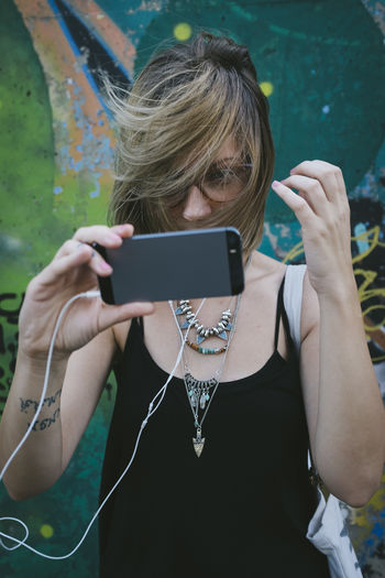 Woman taking selfie from mobile phone with tousled hair against wall