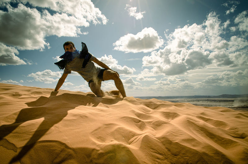 Man climbing on sand dune in desert against sky
