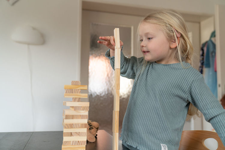 A toddler girl builds a wooden tower on a table
